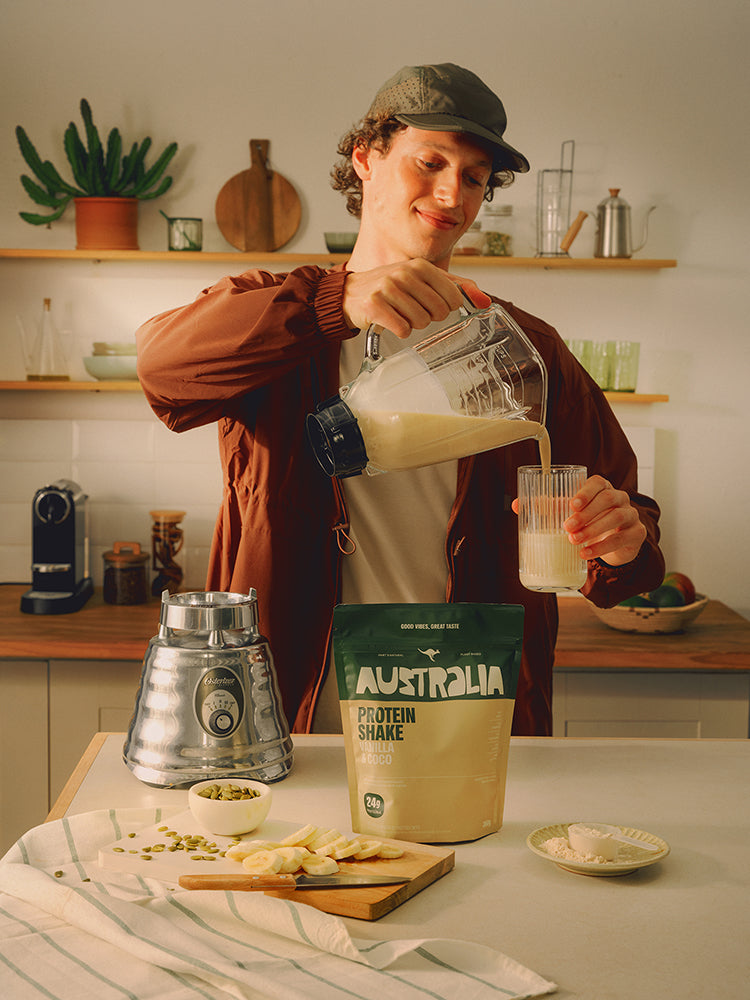 Pessoa prepara um shake em uma cozinha, com uma embalagem AUSTRALIA sobre a bancada.