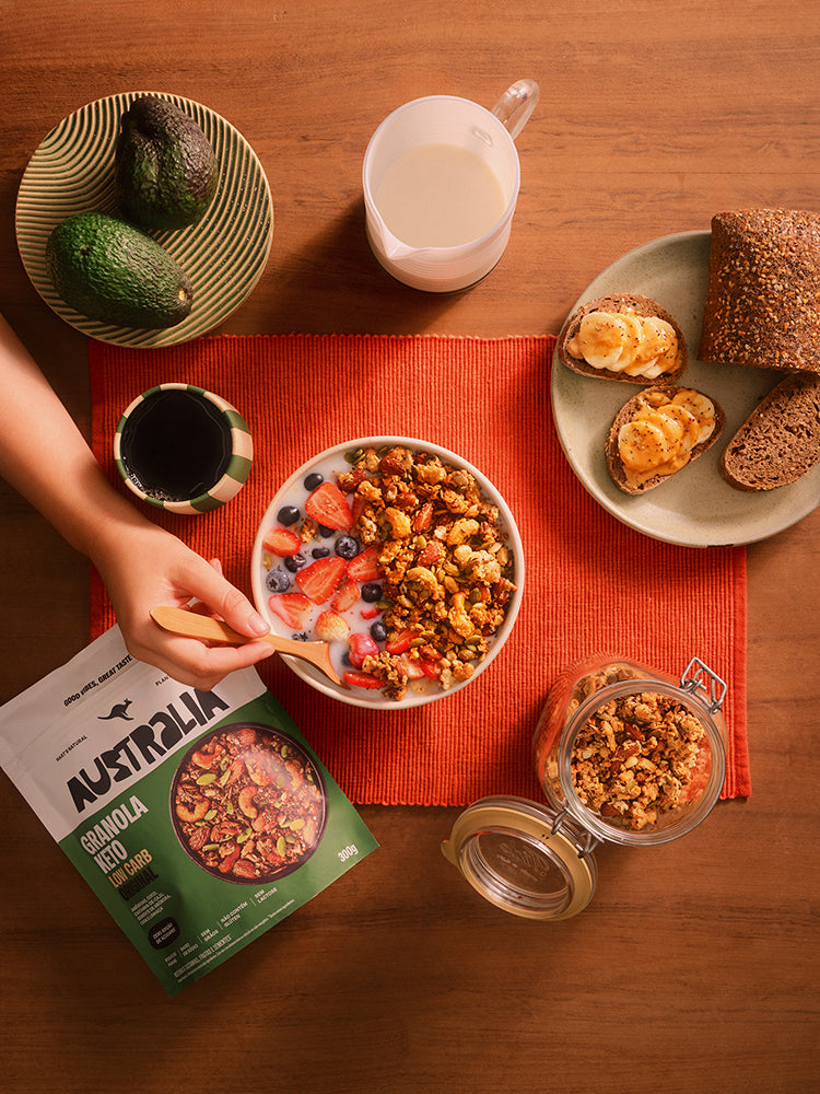 Tigela de granola, frutas e café vista de cima sobre uma mesa de madeira.