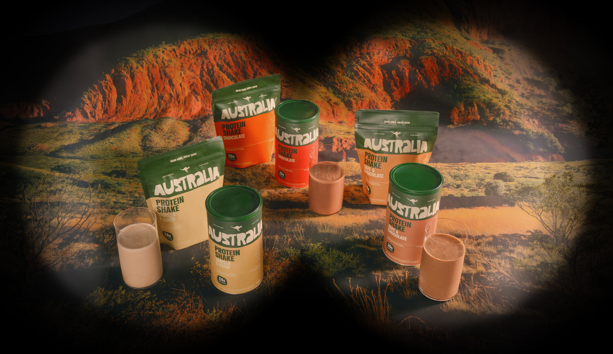 Embalagens e copos de Protein Shake AUSTRALIA diante de uma paisagem de montanha.