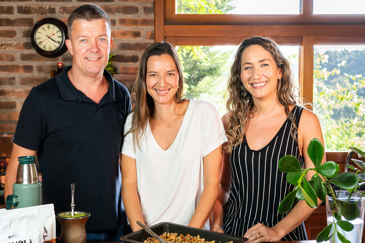 Milo, Raquel e Sabrina sorrindo na cozinha, com uma assadeira de granola na bancada.