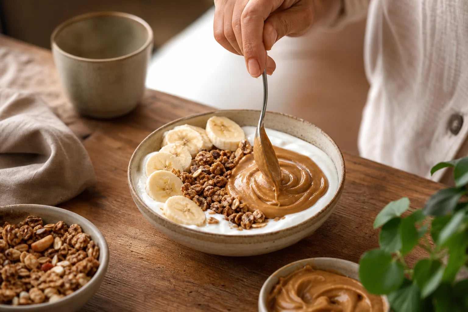 Pessoa finalizando uma tigela de iogurte, banana, granola e pasta de amendoim.