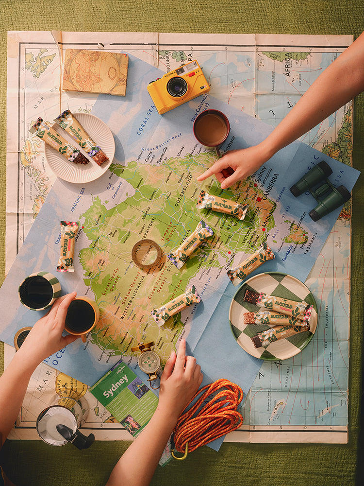 Mãos organizam barras AUSTRALIA e objetos de viagem sobre um mapa.