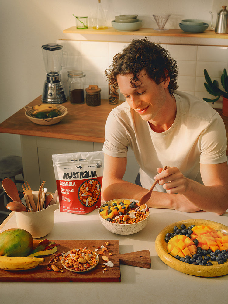Uma mulher despeja leite numa tigela de Granola Classic Nuts com frutas. O pacote está ao lado, na mesa.