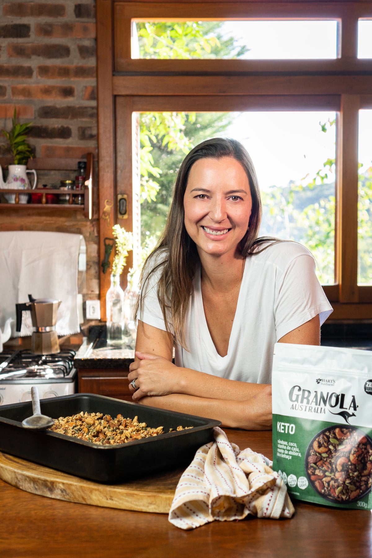 Raquel na cozinha, ao lado de uma assadeira de granola e de uma embalagem antiga.