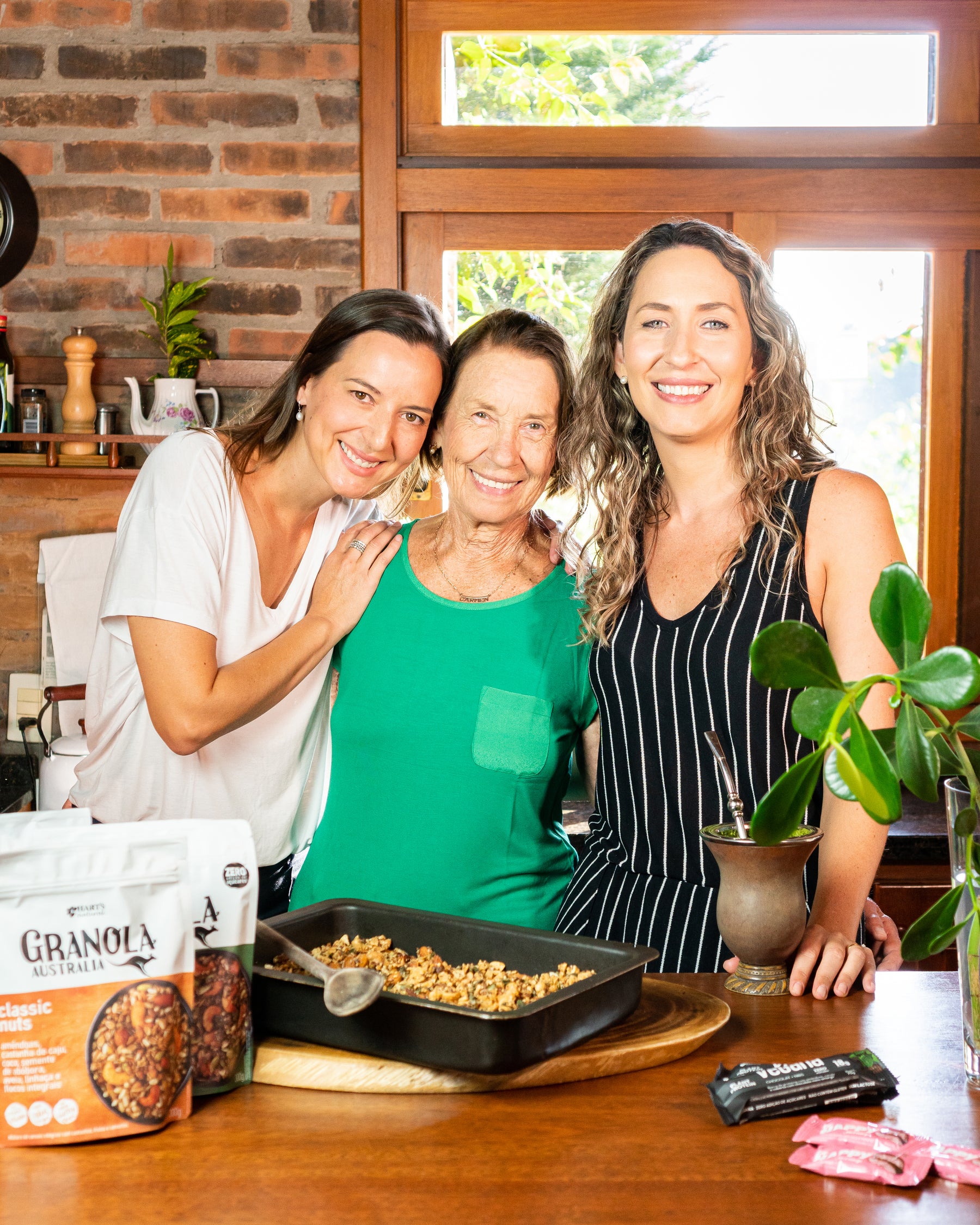 Raquel, Carmem e Sabrina reunidas na cozinha com embalagens da primeira fase da marca.