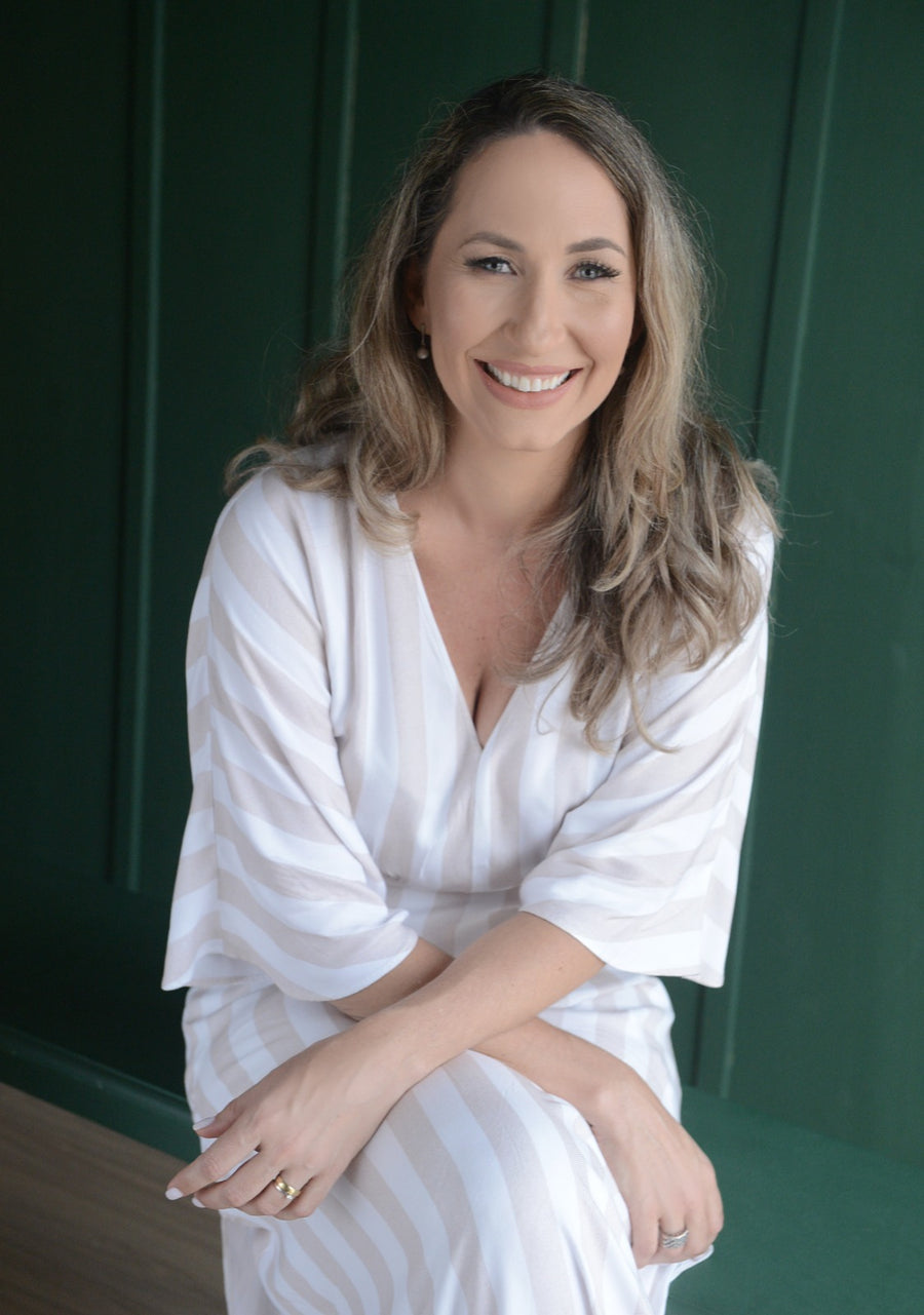 Sabrina sorri, sentada diante de uma parede verde-escura.
