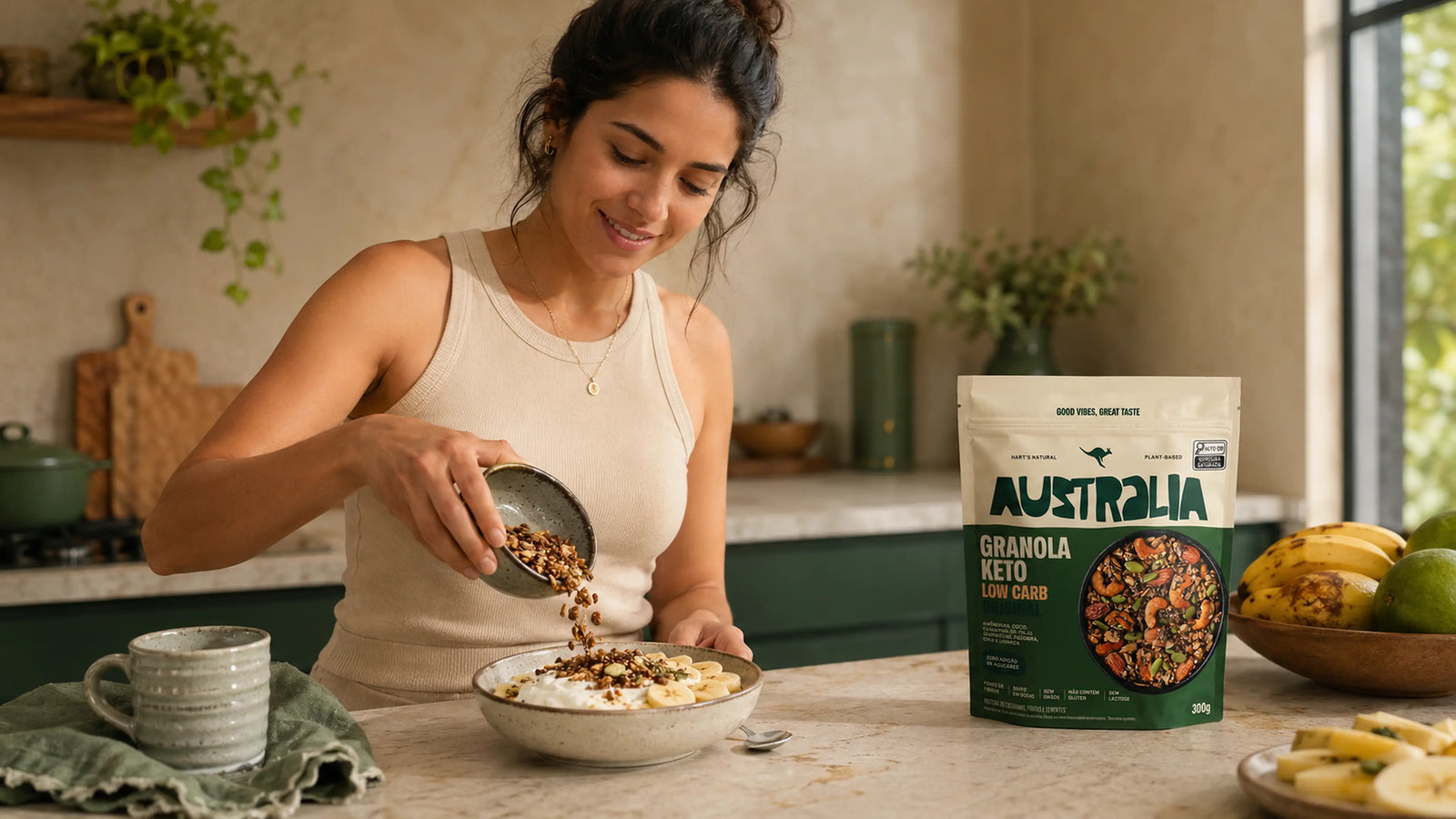 Pessoa servindo Granola Keto Original sobre iogurte e banana em uma cozinha iluminada.